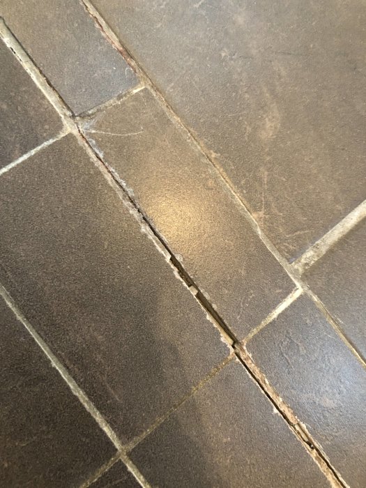 Sprickor och släppt silikon i brun kakelfog i dusch.