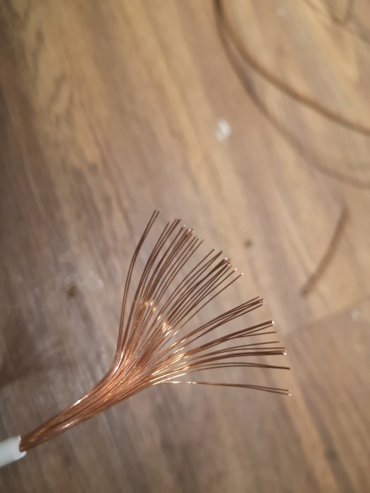 Färgad flertrådig kabel med sju utspridda kopparledare mot träbakgrund.