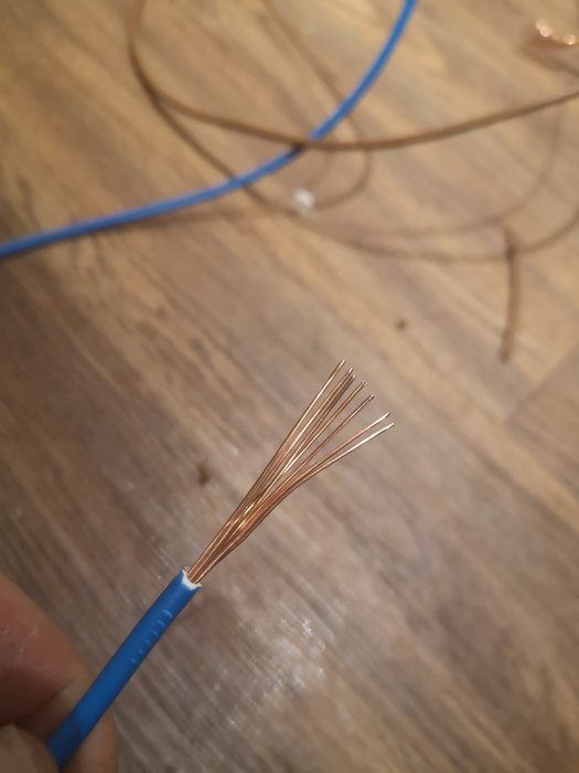 En avskalad blå kabel som visar sju koppartrådar mot en träbakgrund.