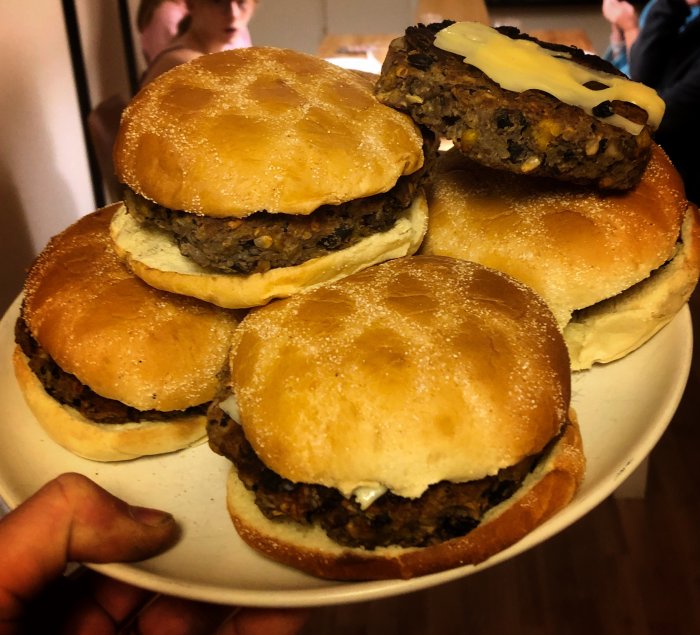 Hand som håller en tallrik med hemgjorda vegoburgare i brödbullar, grillade på Weber-grill.