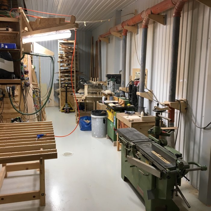 Organiserad verkstad med olika träbearbetningsmaskiner, arbetsbänkar och rörsystem för spånhantering.