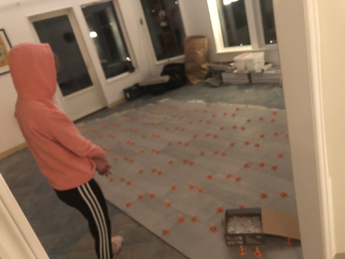 Person i rum med skyddspapp och utspridda orange distansklossar för kakelläggning.