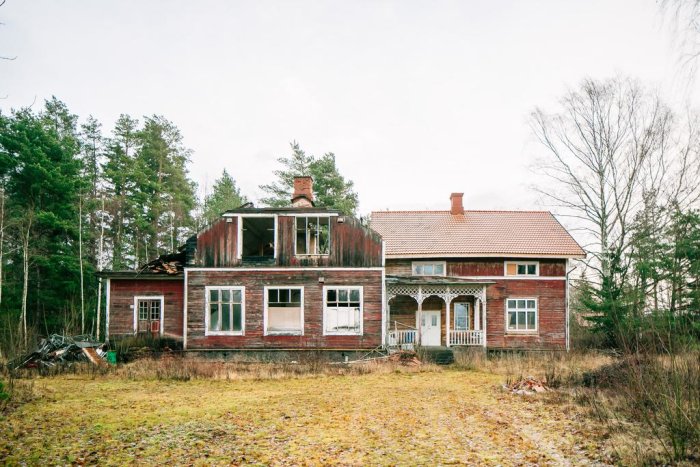 Slitet rött trähus med sönderfallande tak och övervuxen tomt, renoveringsprojekt för den händige.