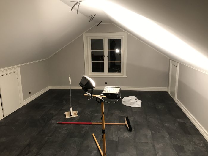 Renoverat loft med mörkt klickgolv, vitmålade tak och väggar samt inbyggda förvaringsluckor.