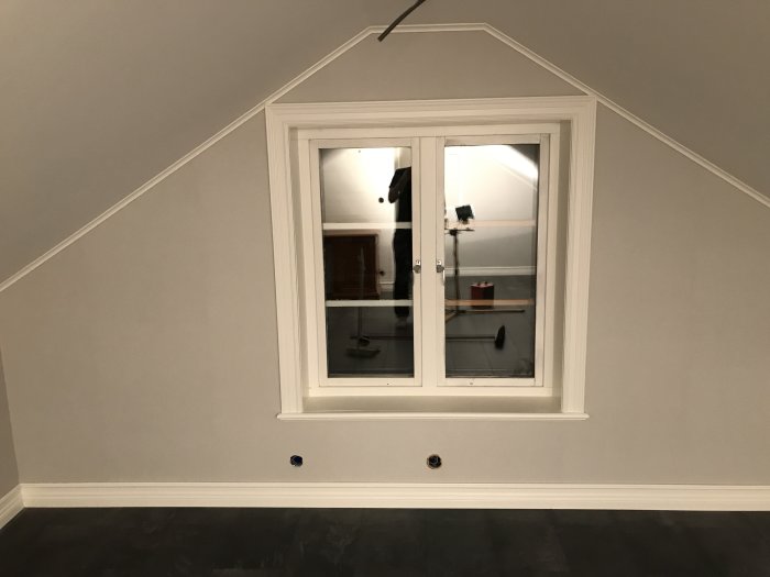 Renoverat loft med målat tak, tapetserade väggar, klickgolv och fönster som visar reflektion av rummet.