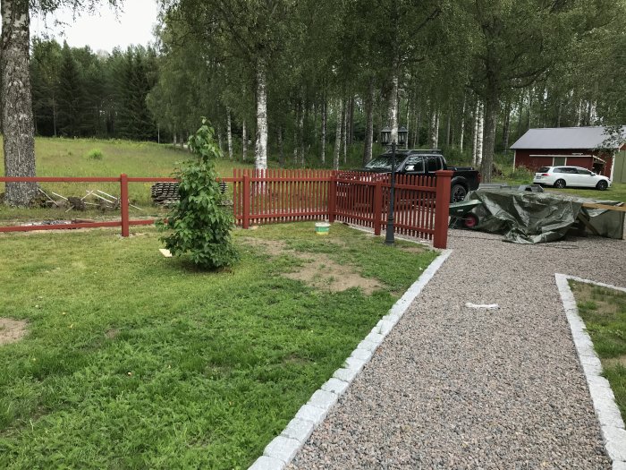 Nybyggt rött staket och oöppnad grind med grusgång och kantsten framför huset.