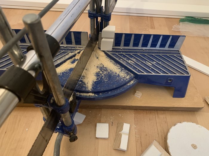 Miter saw set up for cutting with blue base, sawdust, and small white tile fragments on work surface.