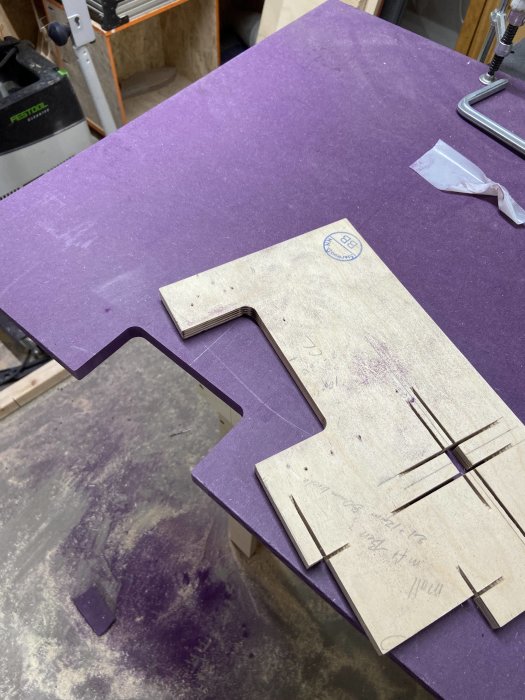 Lila Valchromat-skiva och utskurna delar på arbetsbänk i snickeri.