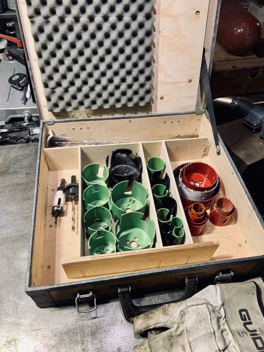 Träverktygslåda öppen med gröna hålsågar, en borr och röda sågar - verktyg för projekt.