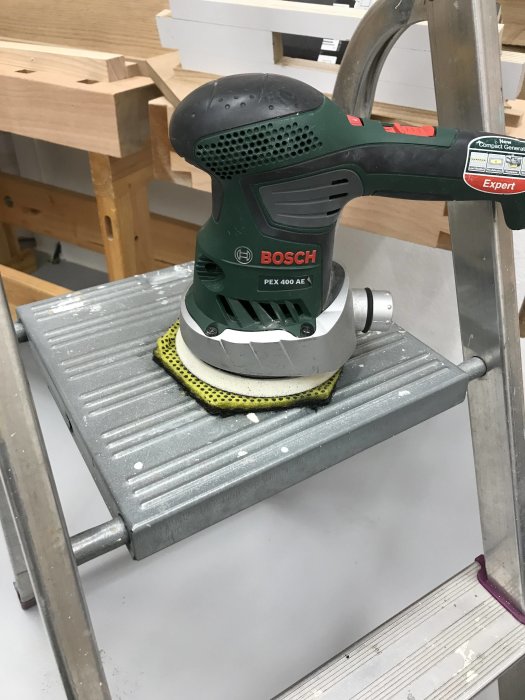 Bosch excenterslip med scotch brite-kuddar på ett slipat bordsågsbord med limrester.