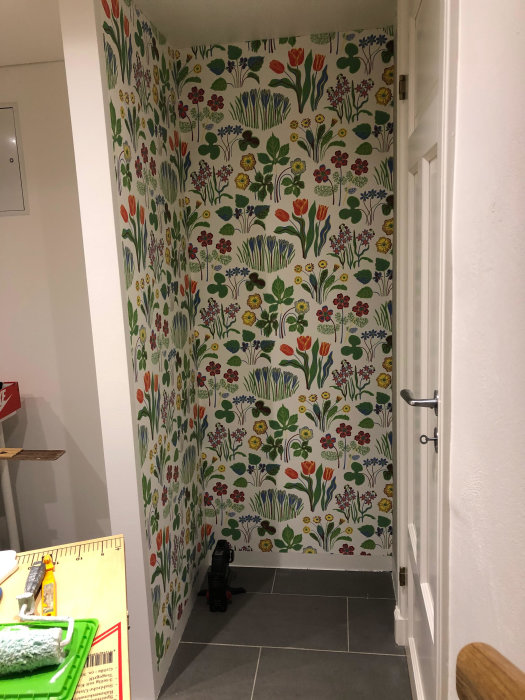 Färgglad blommönstrad tapet monterad på vägg i ett hus med tapetverktyg i förgrunden.
