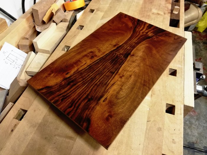 Oljad träpanel med dramatisk ådring på snickarbänk, fällts in gångjärn, omgivet av verktyg och träbitar.