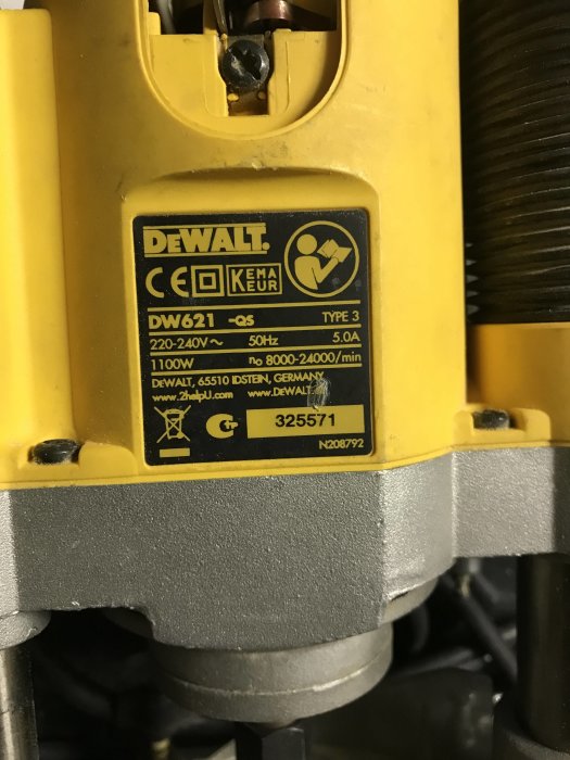 Närbild på en DeWalt DW621 fräs med specifikationsetikett och synlig skada där plast smultit vid kolet.