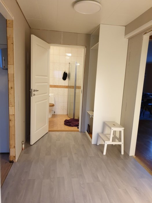 Renoverad hall med nytt laminatgolv, vita trösklar och nyligen installerade gipsskivor på väggar inför målning.