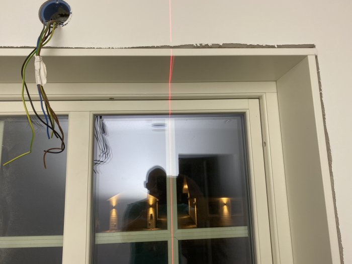 Fönstersmyg under renovering med laserlinje, synliga kablar och icke färdigställd vägg.