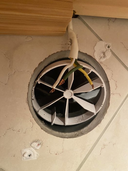 Öppen badrumsfläkt i taket med oskyddade grön, vit och gul kablar i ett oavslutat kopplingsjobb.