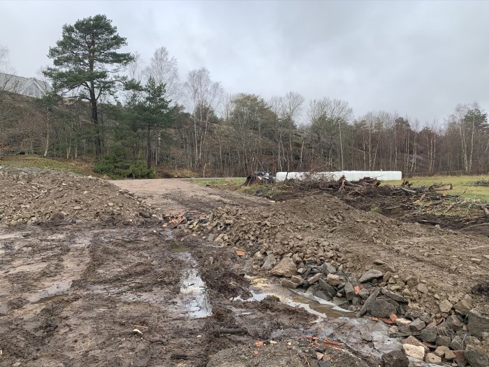 Vägbygge med sten och grus, lerigt markarbete, och rör synligt för elslang under planen.