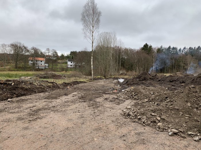 Markarbete med sten och jord, ny väg och plan yta under anläggning, natursköna omgivningar i bakgrunden.