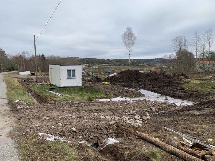 Markarbete för vägbygge med grus, en elslang och en byggbod på en byggarbetsplats.