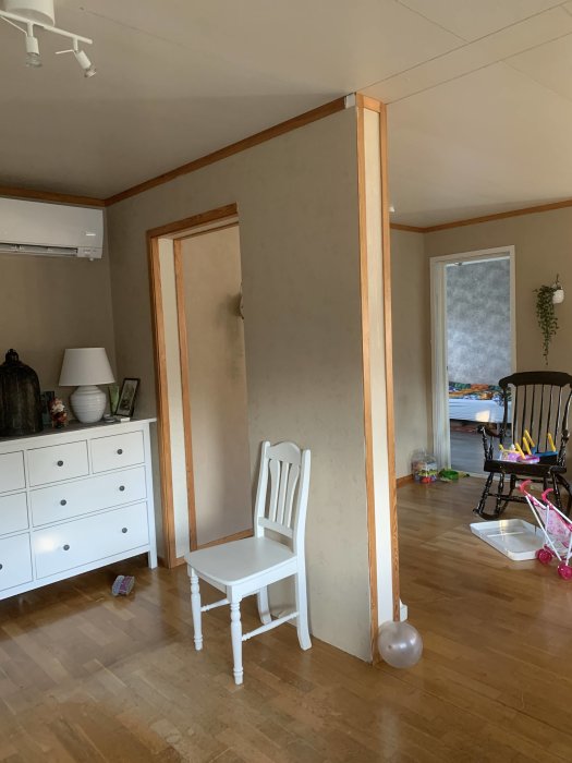 En del av vardagsrummet med en bärande väggsnutt som går från golv till tak, med början av en öppning mot ett annat rum.