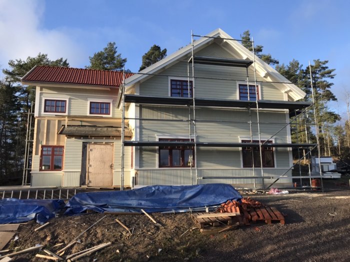 Hus under renovering med ställning, nästan färdig fasad på framsidan och byggmaterial framför.