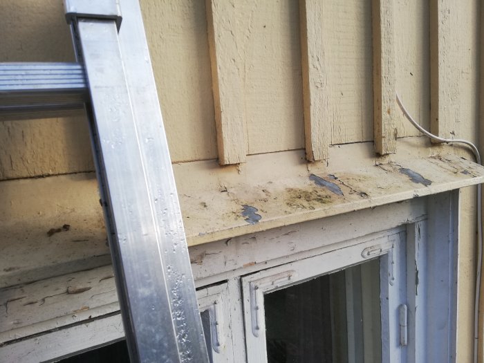 Våt träpanel och fönsterkarm med tecken på vatteninträngning på ett äldre hus.