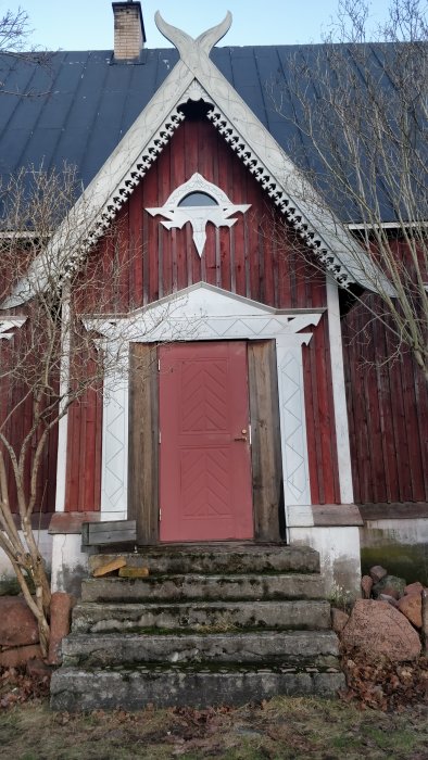 Kultur-märkt kapell med karaktäristiskt träsnideri och en röd dörr, uppfört 1921, i behov av renovering.