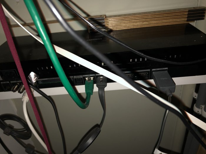 Multimediautrustning och kablar i en box under TV med en grå kabel till höger.