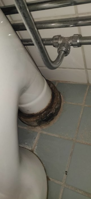 Närbild på anslutningen mellan en toalettstol och avloppsröret, med synlig slitage och rörledningar överst.