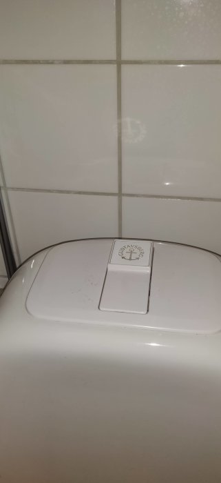 Sliten Gustavsberg Nordic WC-stol med synlig logotyp, mot kakelvägg.