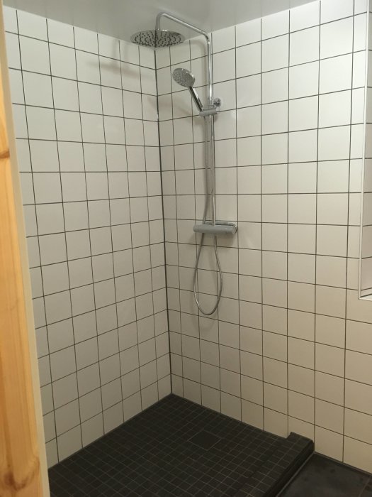 Nyrenoverad duschhörna med kaklade väggar, takdusch och handdusch samt mörk klinkergolv.