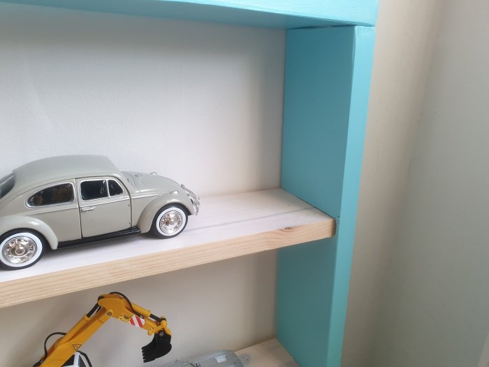 Hylla av MDF i ett hörn med leksaksbil och leksakskran, ommålad och ska dekoreras.