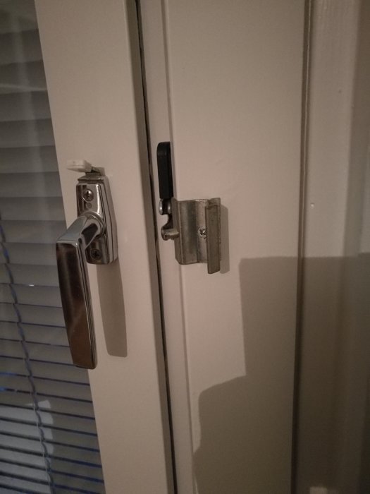 Vit vädringslucka med öppet metallbeslag på höger sida och handtag till vänster, beslagets "pegg" saknas.