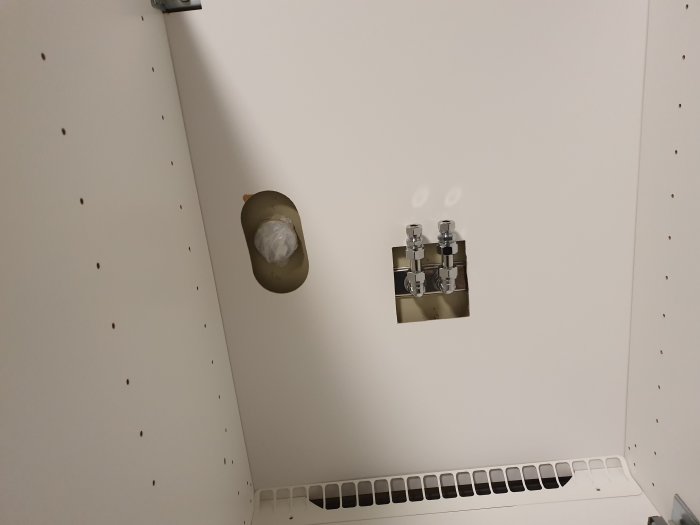 Installation av VVS med exponerade rör och pluggat hål på en vägg med gipsskivor och golvventil.