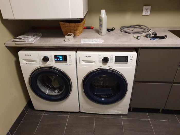 Tvättstuga med nyinstallerad vit Samsung tvättmaskin och torktumlare under arbetsbänk.