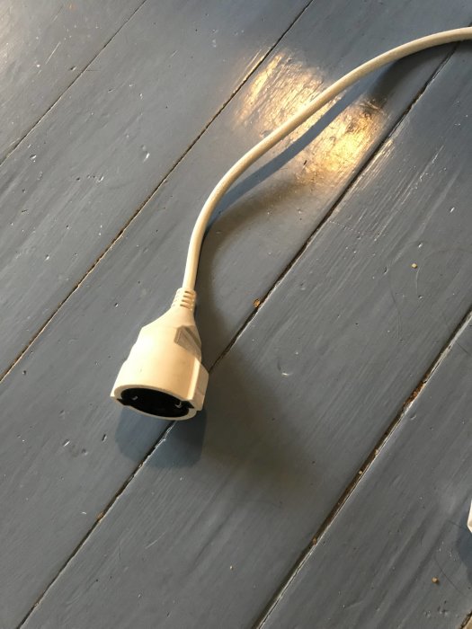 Lös lampa med stickkontakt ligger på ett grått trägolv.