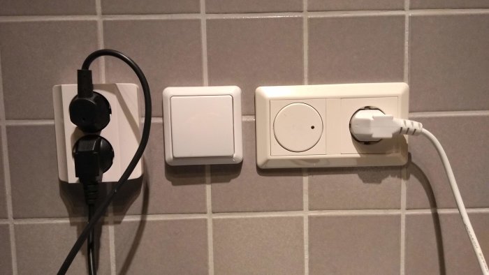 Vägguttag och timer i kök med inkopplade stickproppar och sladdar mot kakelvägg.