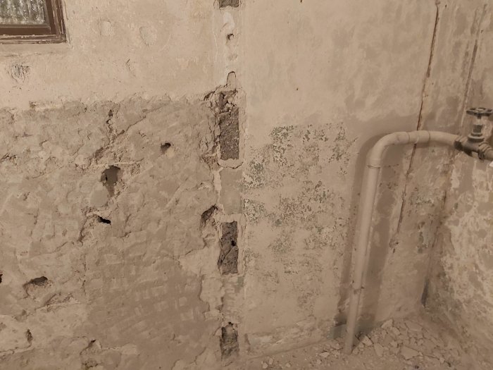 Renoveringsprojekt av en tvättstuga med avhackad puts och gammal färg på betongväggar och rörinstallationer.