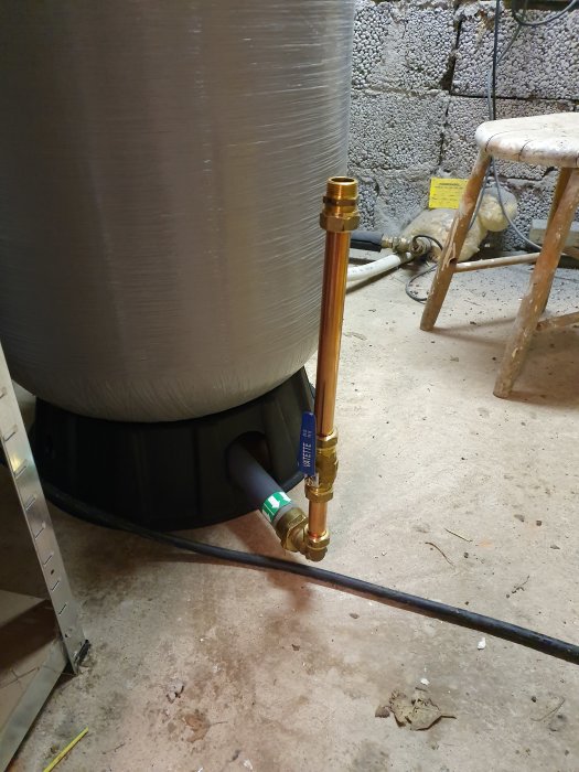 Hydrofor och kopparledningar för vattenfiltrering installerade i källare med betongvägg och golvbrunn.