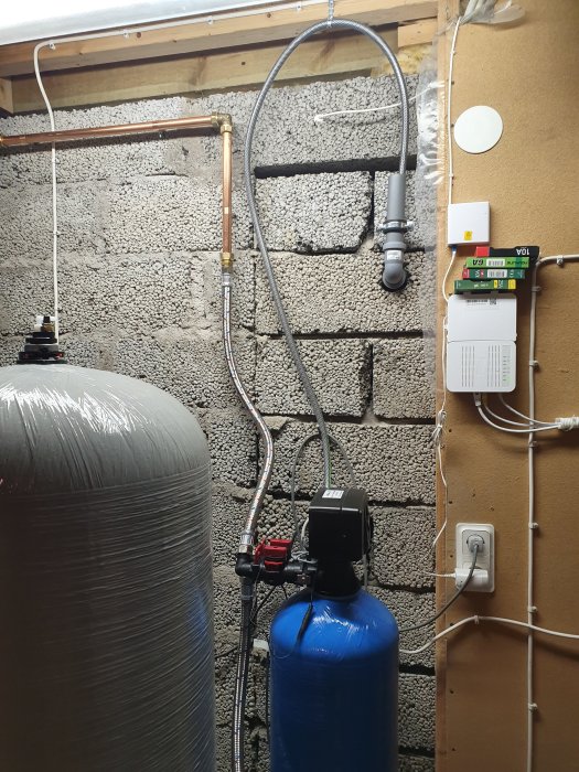 Vattenreningsfilter och hydrofor i källare med rörinstallationer och elektronisk kontrollenhet.