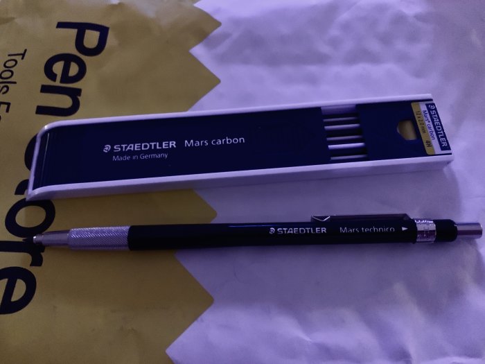 Staedtler Mars technico stifthållare och en låda med Mars carbon stift på en guldgul yta.