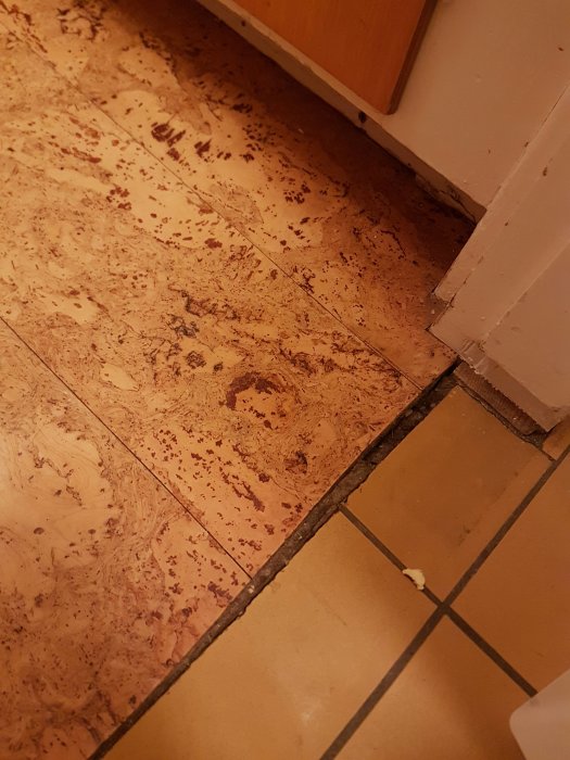 Gammalt slitet köksgolv med mönstrad plast/korkmatta möter beige kakel, potentiell asbestfråga.