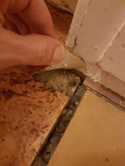 Hand lyfter korkmatta i hörn av rum för att visa möjligt asbesthaltigt material under.