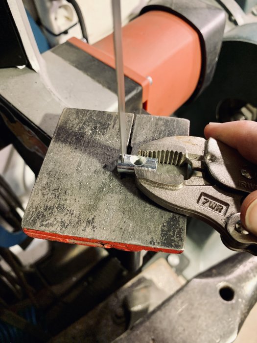 Hand som håller en tång som reparerar ett metallbeslag på en arbetsbänk.