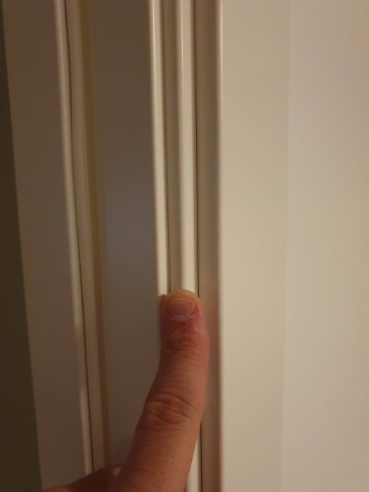 En hand som visar vita lister mot en vägg, illustrerar renoveringsarbetet med renoveringsgips.