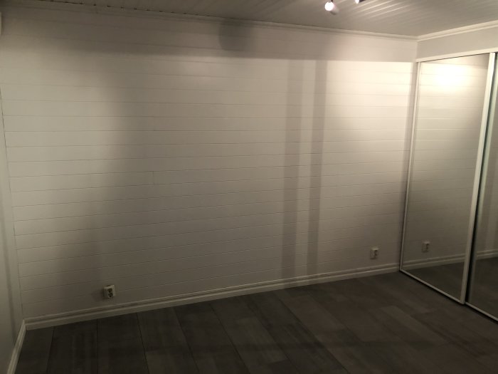 Nylagd panelvägg och golv i ett sovrum med speglade skjutdörrar till garderob.