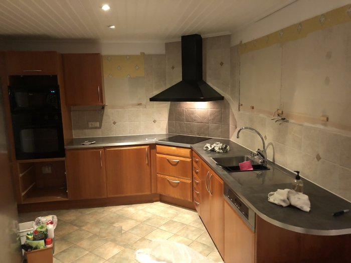 Kök under renovering med borttagna överskåp och framträdande väggplattor.