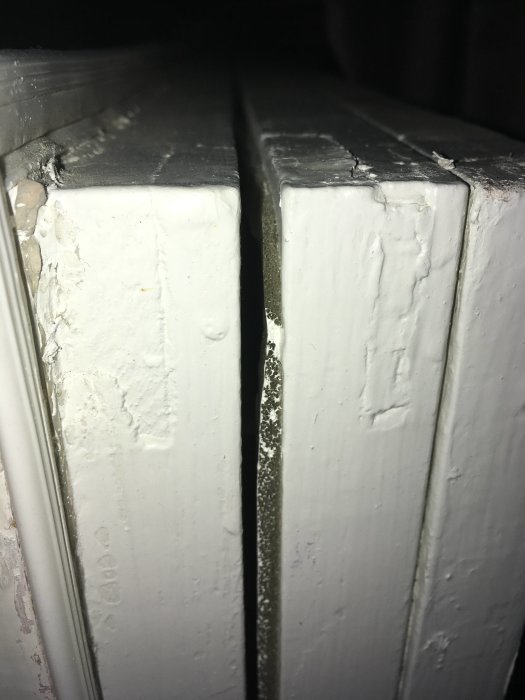 Närbild på en vit fönsterkarm med slitage och sprickor mellan två delar.