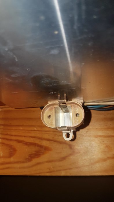 Transparent lampsockel monterad på träyta med öppna kabeländar synliga, avsedd för byte eller reparation.