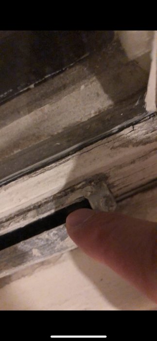 Närbild på gammal fönsterventil mellan karmen och väggen, finger pekar på osynliga skruvar.